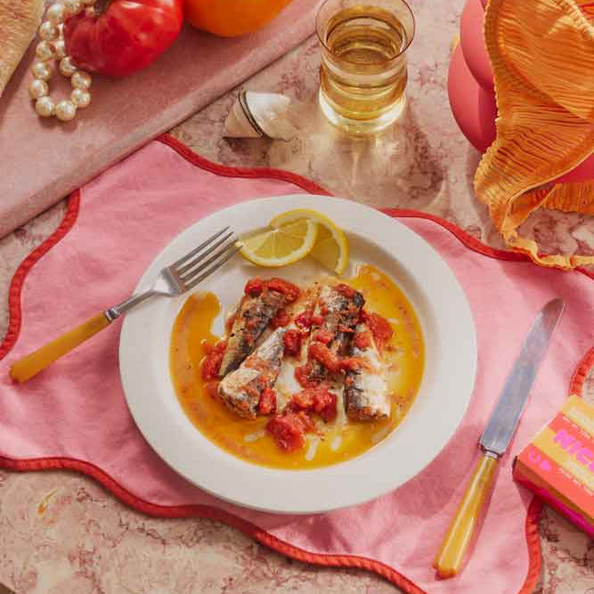 Dish of fish with lemon wedges on a table with a glass of wine and colorful decor.