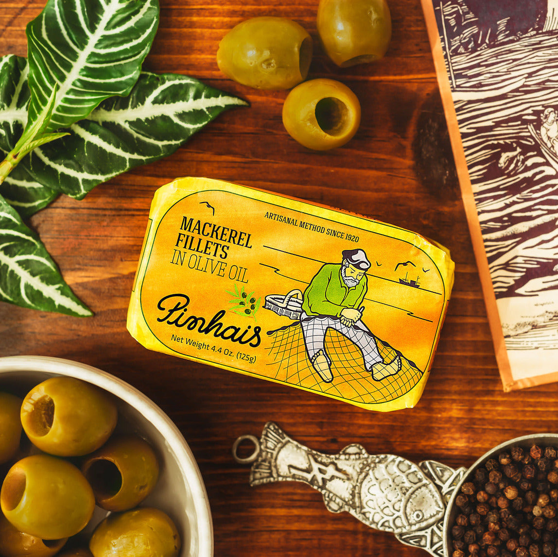 Pinhais mackerel fillets in olive oil packaging on a wooden surface with olives and a book.