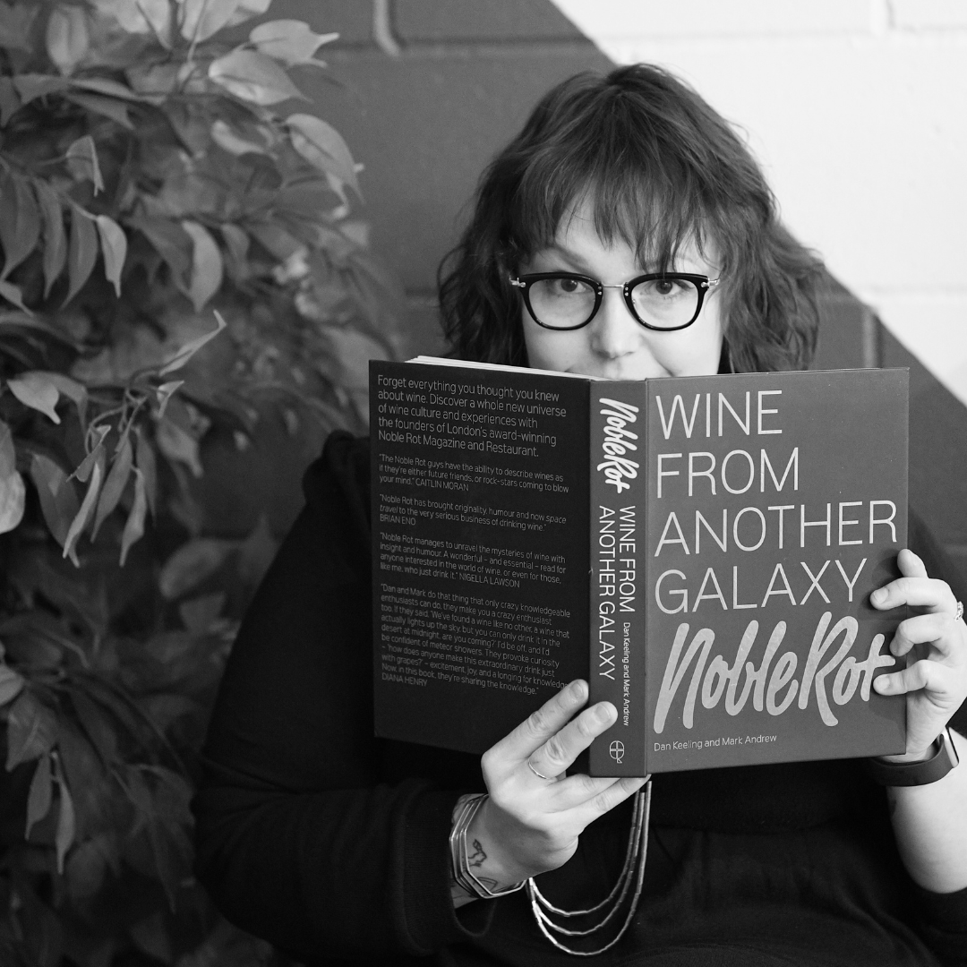 Cara Patricia seated, peeking out from behind a wine book